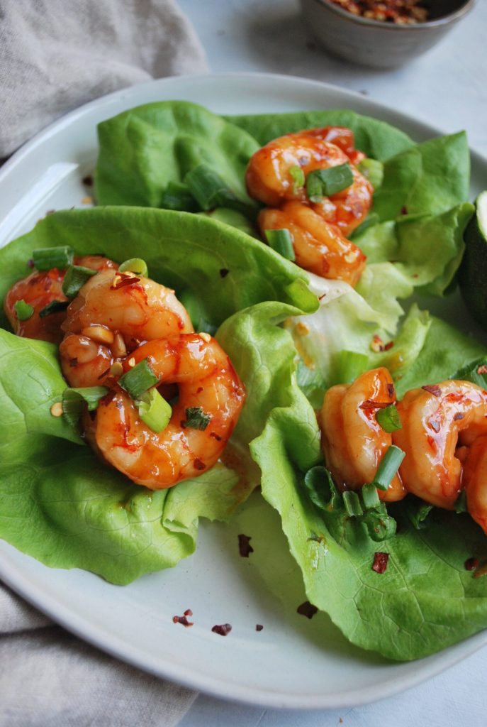 Sweet and sour shrimp lettuce cups close up on a white plate.