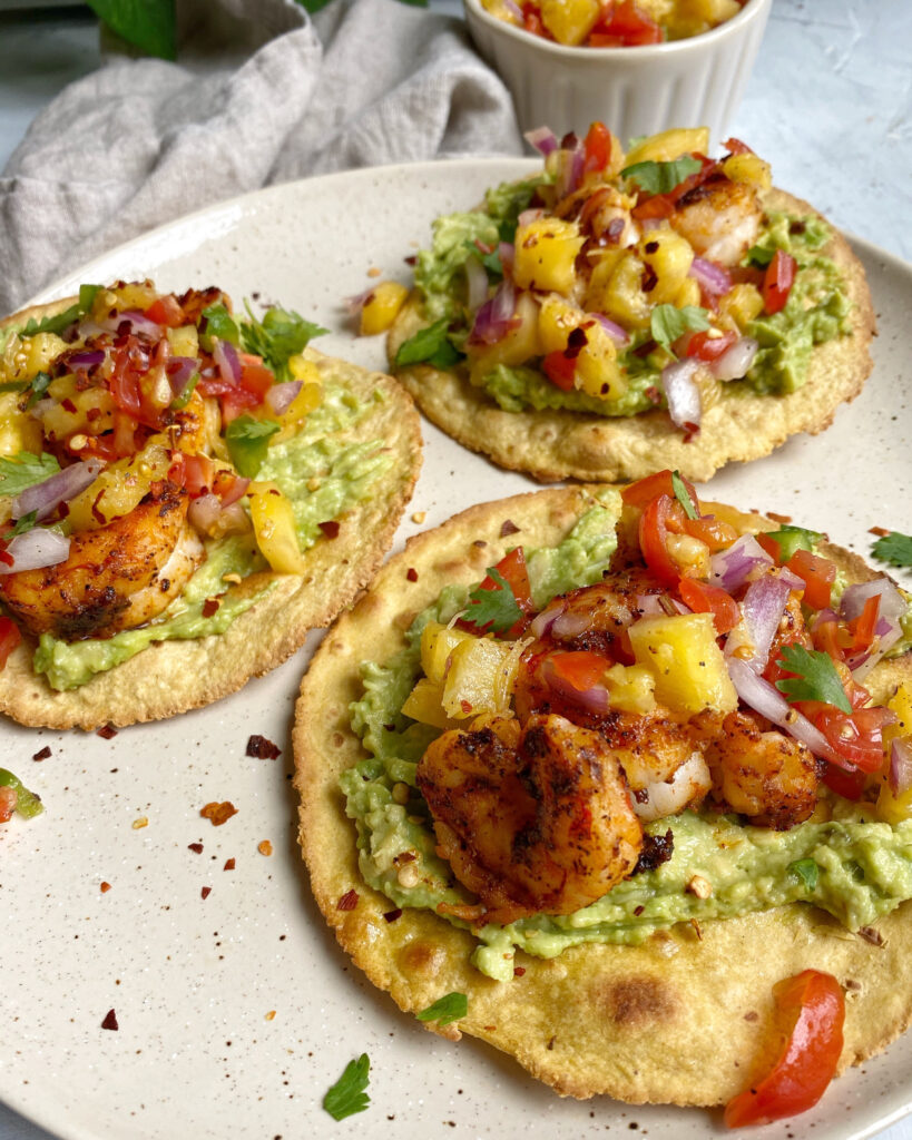 Close up of shrimp tostadas with smashed avocado and pineapple salsa on a white plate.