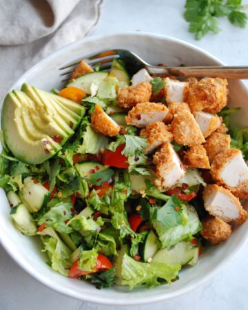 Close up of a Buffalo Chicken Chopped Salad with cubed chicken pieces and a slice avocado in a white bowl with a fork on the side.